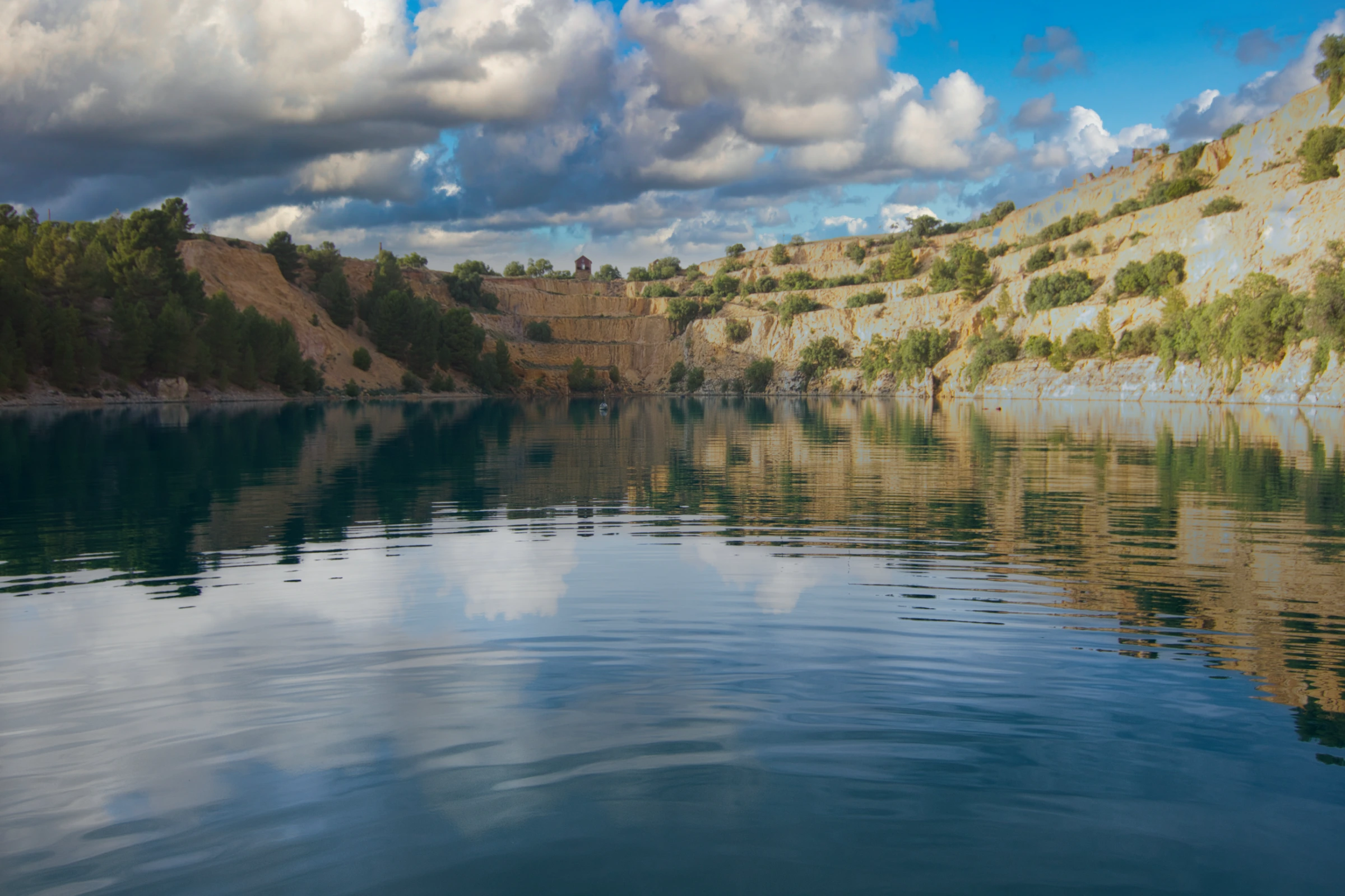 The flooded Burra quarry training site, sheer ochre cliff faces reflected in calm green water under a clouded sky